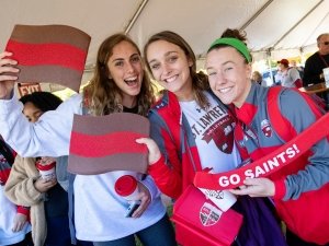 Three Saint Lawrence University students wear and hold up scarlet and brown school spirit items.