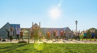 A yoga instructor guides a group of people through stretches on the Saint Lawrence University quad during a sunny day.