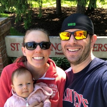 Jack '11 and Emily Tulip Droppa '09 with baby in front of St. Lawrence campus sign