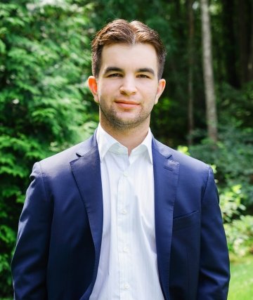 Headshot of Bobby Tremont, wearing a white collared shirt and a navy blazer, standing in front of a leafy wooded background.